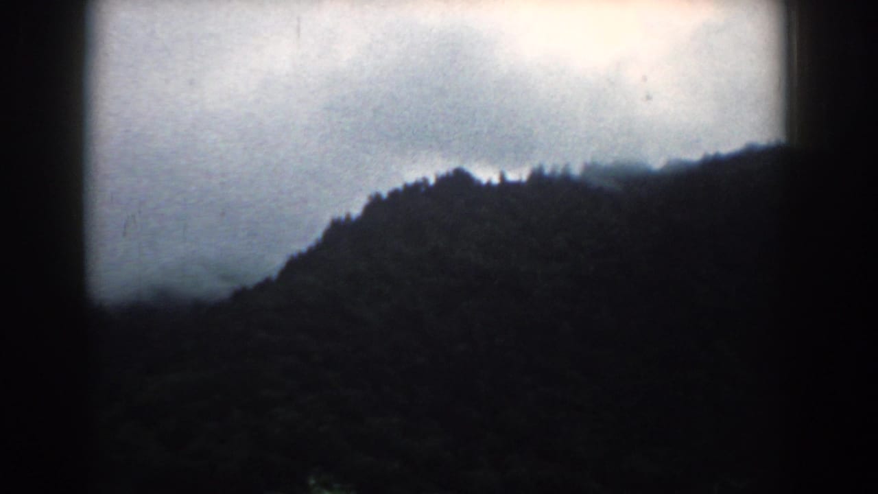 1958 South Carolina 8mm frame showing a shadowed wooded ridge under an overcast sky, with soft focus and dark film borders.