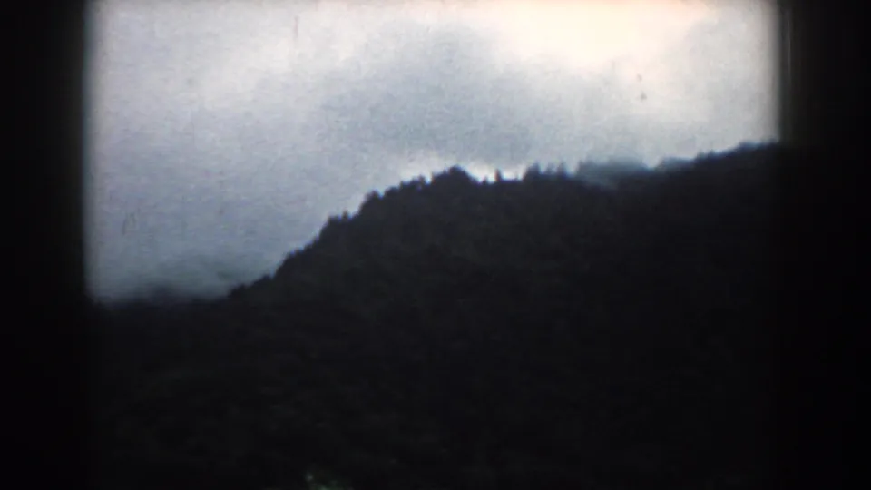 1958 South Carolina 8mm frame showing a shadowed wooded ridge under an overcast sky, with soft focus and dark film borders.