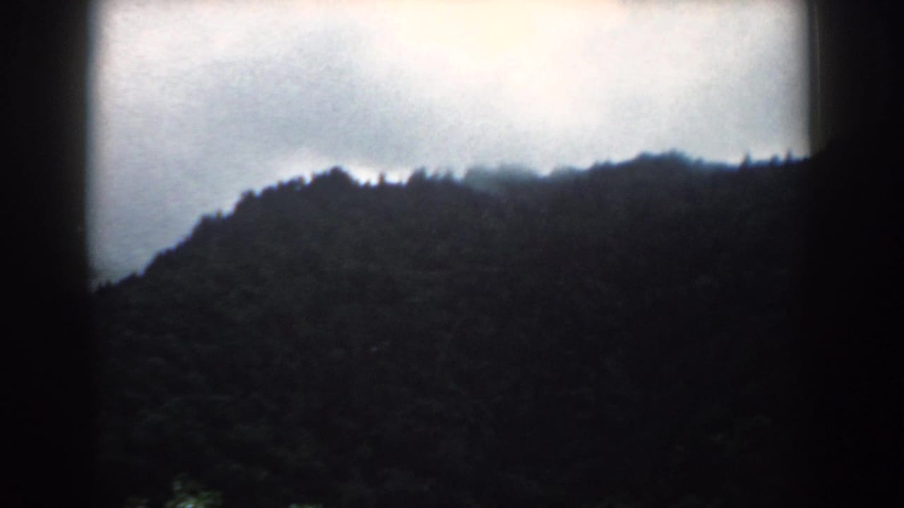 Wide view of a silhouetted wooded ridge under bright overcast clouds.