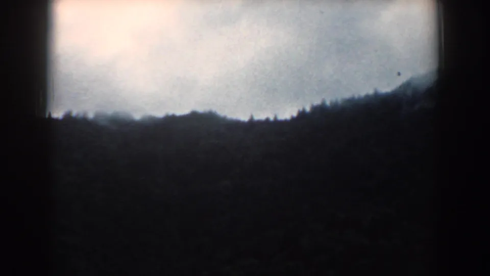 1958 South Carolina 8mm frame showing a dark forested ridge beneath an overcast sky, bordered by deep black film edges.