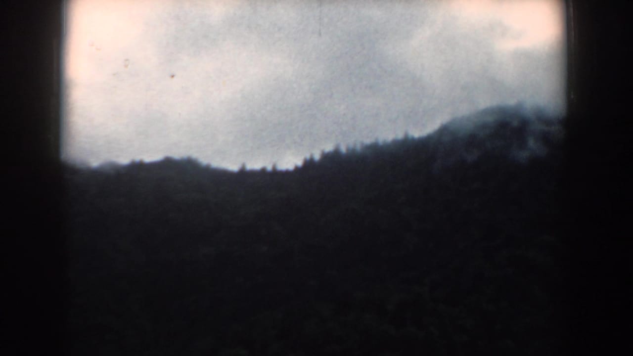 Shadowed mountain ridge with low clouds and a bright overcast sky above.