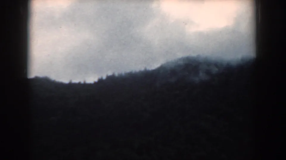 1958 South Carolina 8mm frame with dark wooded hills below a bright, cloud-filled sky and soft film texture.