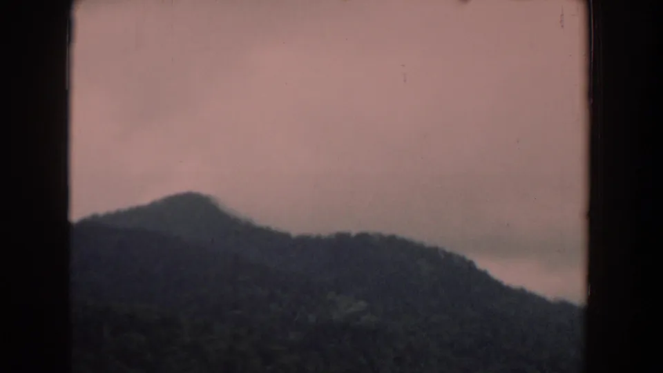 1958 South Carolina 8mm frame showing a dark mountain ridge with mist or low cloud beneath a pinkish sky.