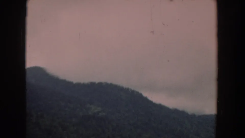 1958 South Carolina home-movie frame of dark rolling hills beneath gray clouds, seen through a black vertical frame.