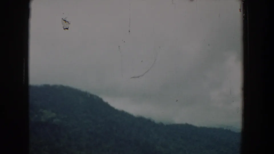 1958 South Carolina home-movie frame showing a dark hillside under gray cloud cover with visible scratches and specks on the film.
