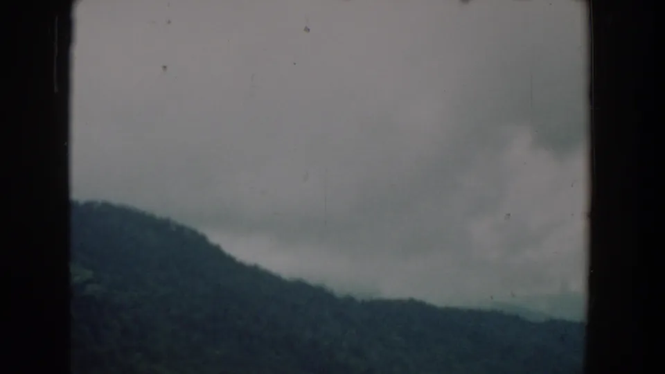 1958 South Carolina 8mm frame of rolling wooded hills beneath thick gray clouds, framed by dark film edges.