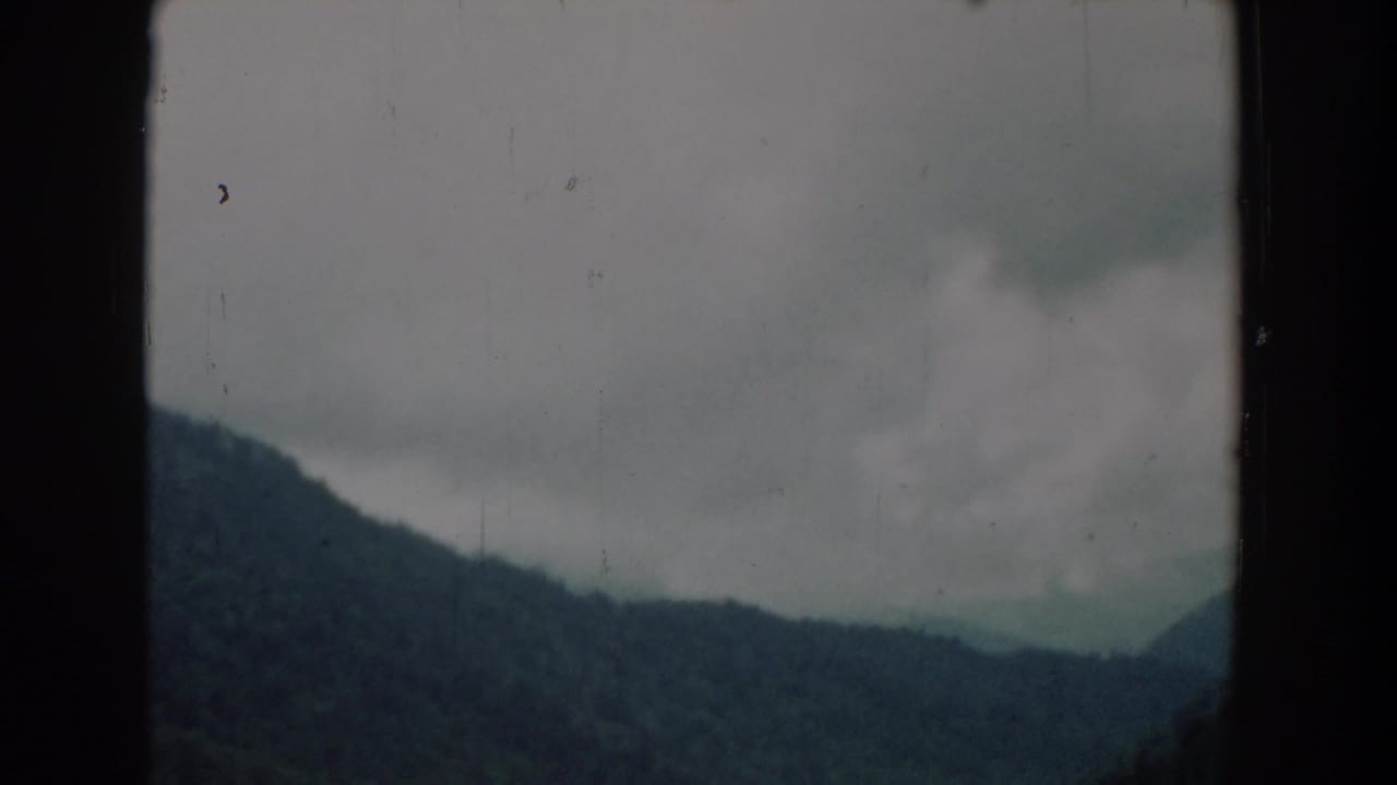 Distant forested ridge and low clouds seen through dark film borders.