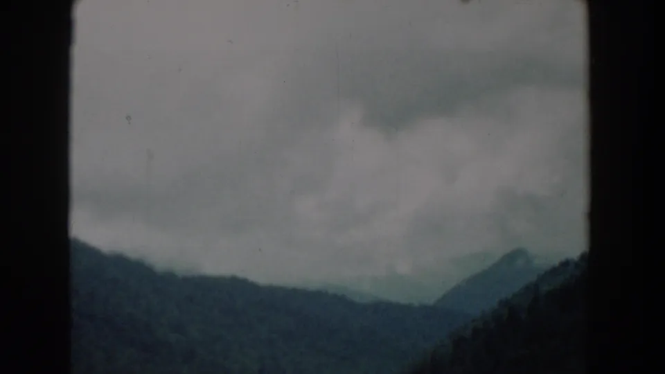 1958 South Carolina home-movie frame with wooded ridges, a distant pointed hill, gray clouds, and visible 8mm gate borders.