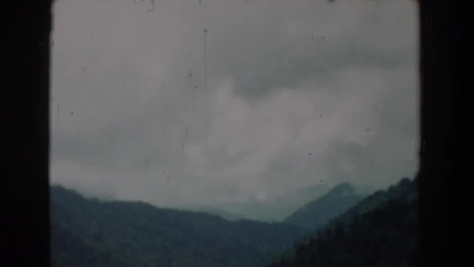 1958 8mm frame showing cloudy mountain ridges and forested slopes, likely from a moving visitor viewpoint.