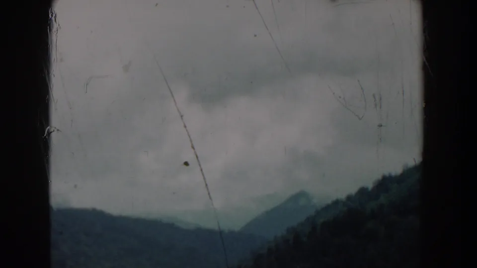 Muted 8mm view of mist over forested mountains, with visible film wear and a dark gate edge.