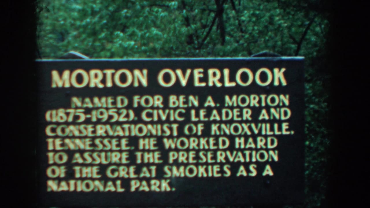 1958 8mm frame of the Morton Overlook sign honoring Ben A. Morton, seen against dense green foliage.