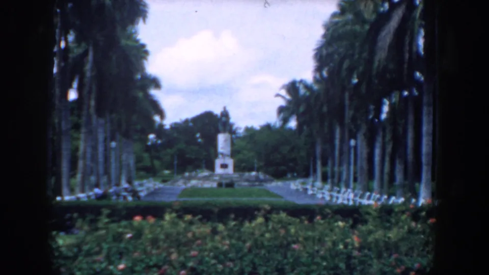 The final frame holds on the same South Carolina garden vista, with dark film edges, palms, benches, hedges, and a distant monument.