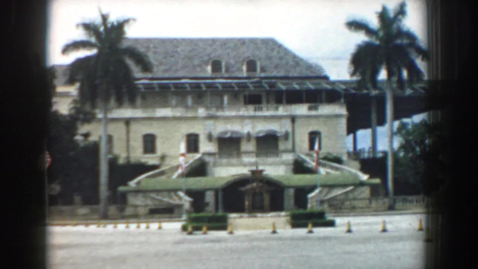 A home-movie view shows a light-colored building with palm trees, stairs, awnings, trimmed hedges, and an open paved foreground in South Carolina.