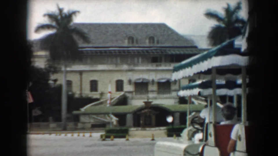 1958 South Carolina 8mm view of a tan multi-story building with palms, striped awnings, an entrance canopy, and an American flag.
