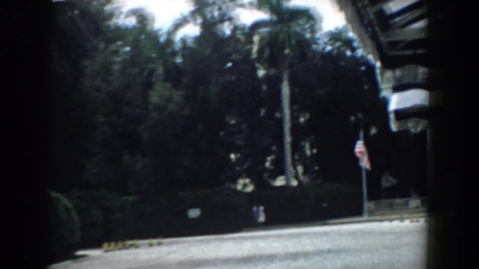 Late in the 1958 South Carolina clip, the view favors palm trees, shaded landscaping, curb markers, and a striped awning at frame edge.