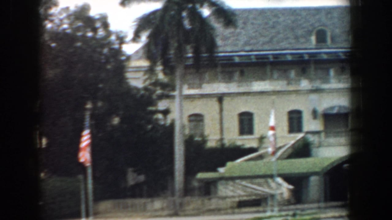1958 South Carolina home-movie frame with a tiled-roof building, palm tree, flagpole, and green awning seen through dark framing.
