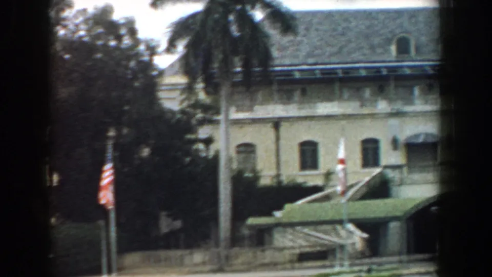 1958 South Carolina home-movie frame with a tiled-roof building, palm tree, flagpole, and green awning seen through dark framing.