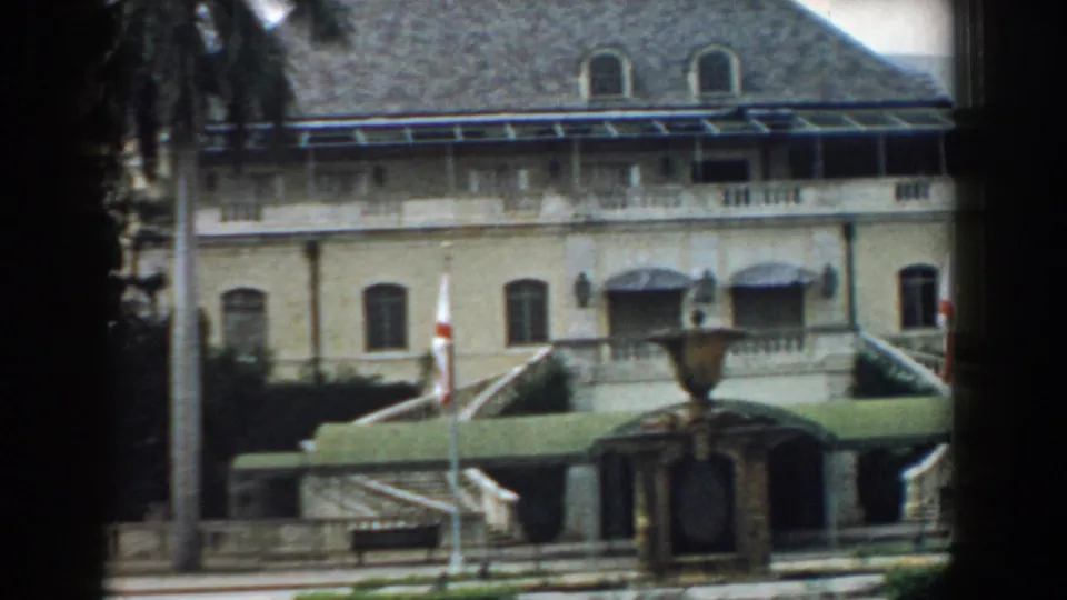 1958 South Carolina frame showing the building facade with arched windows, flags, green awnings, a fountain, and entrance stairs.