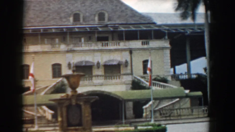 1958 South Carolina 8mm frame showing a formal facade, fountain, flags, green awning, stairs, and dark window-frame edges.