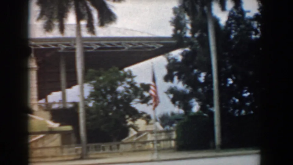 1958 South Carolina travel frame showing palm trunks and a shaded coastal property frontage with awnings, stairs, shrubs, and road edge.