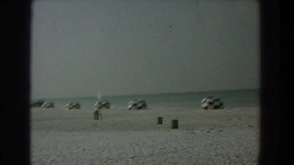 Yorktown beach scene from a 1958 8mm home movie, showing checkered umbrellas, open sand, and calm water.
