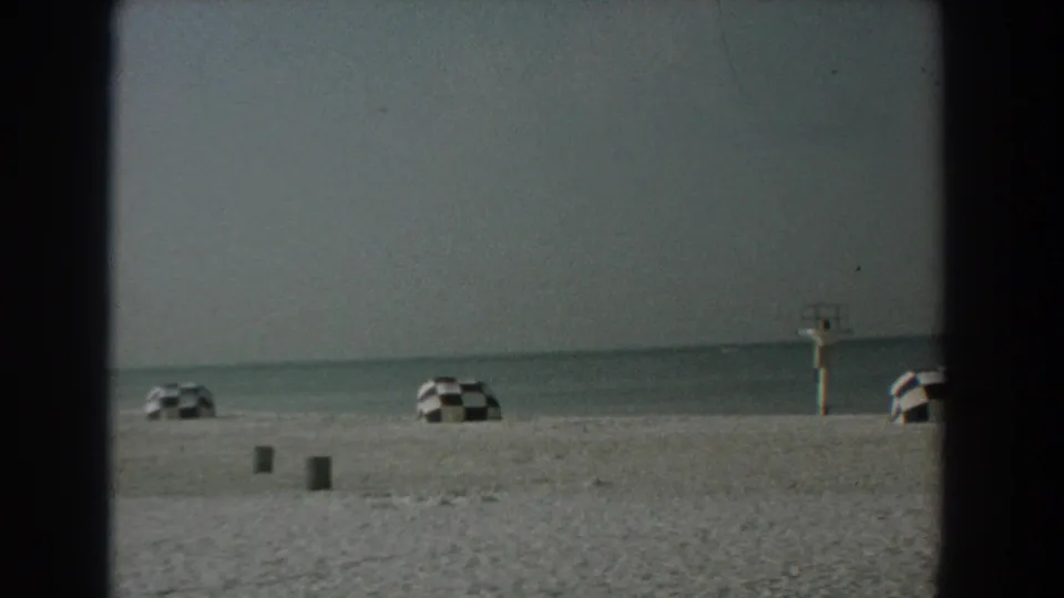 Yorktown, Virginia beach in 1958 with a distant lifeguard stand, checkered umbrellas, sand, and calm sea.