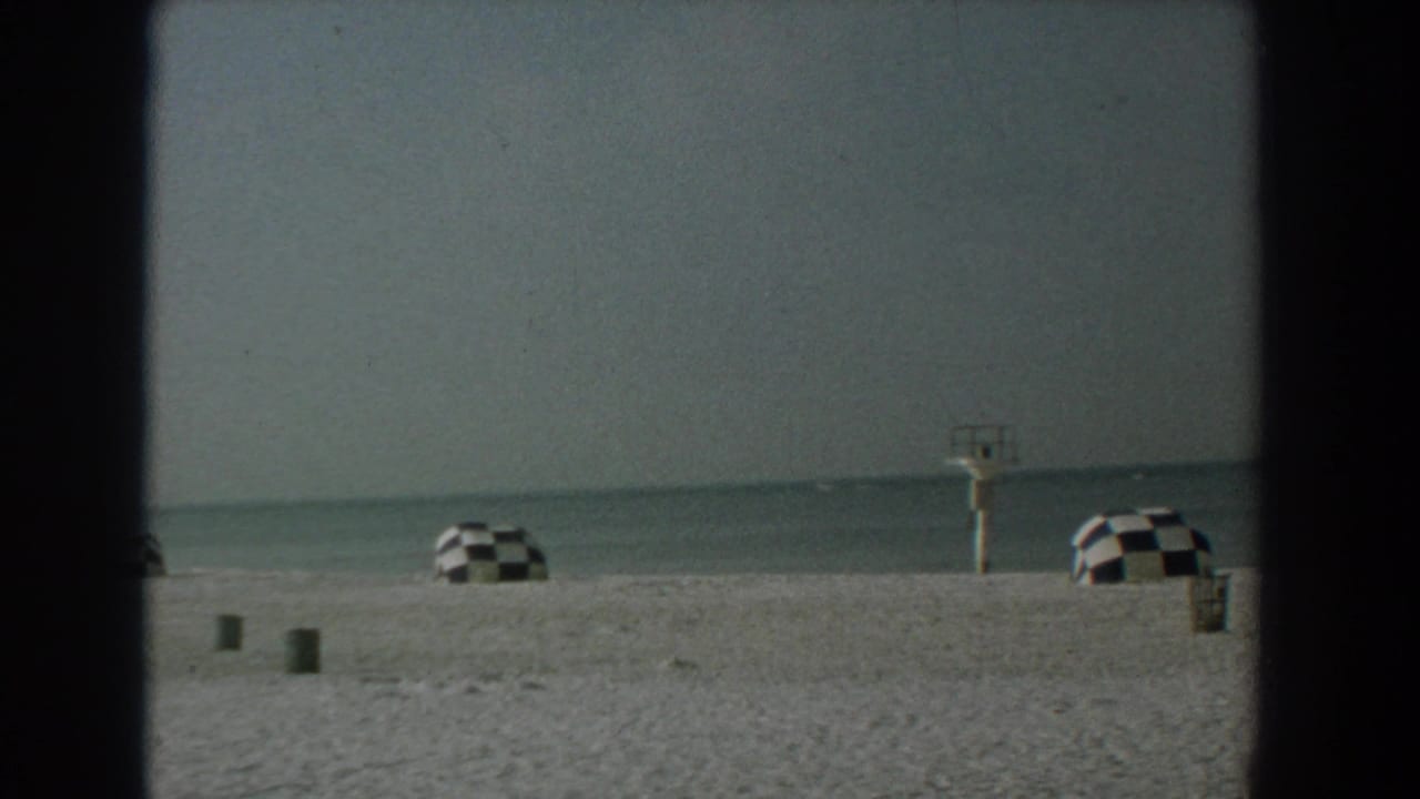 Empty sandy beach with two checkered umbrellas, calm water, and a small lifeguard stand.