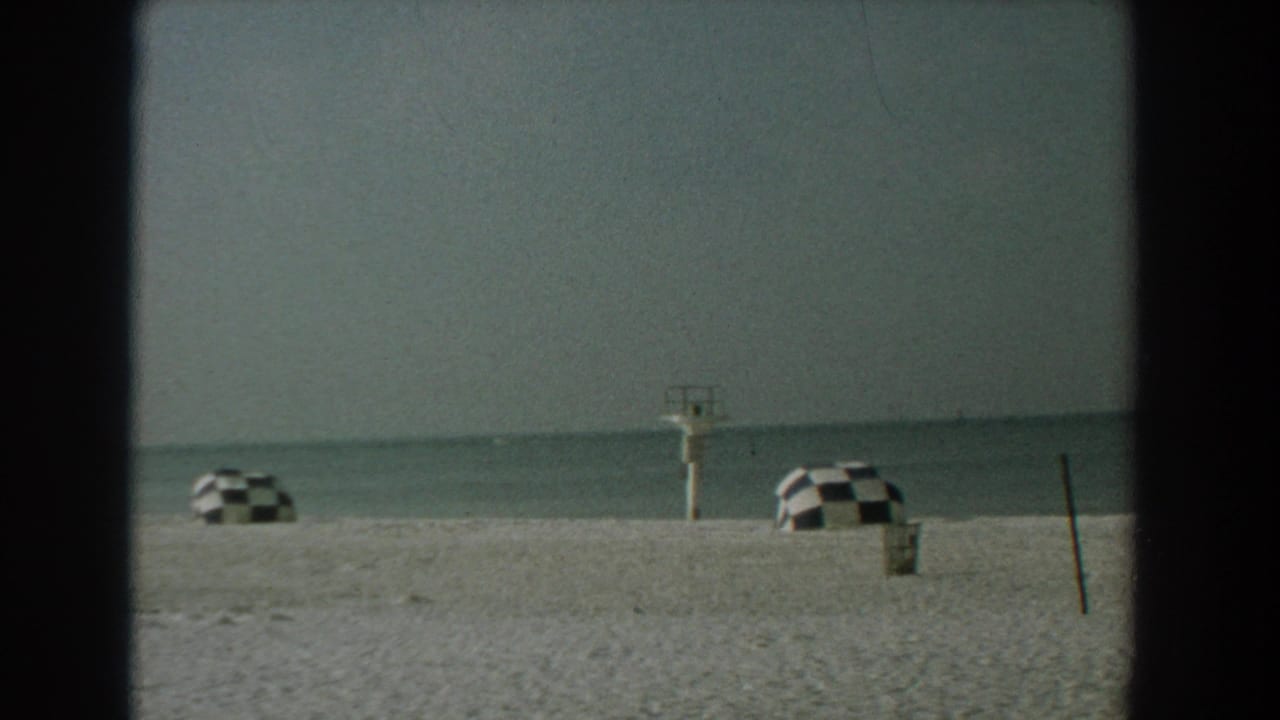 Wide beach view with two checkered umbrellas, waterline, lifeguard stand, and a dark edge border.