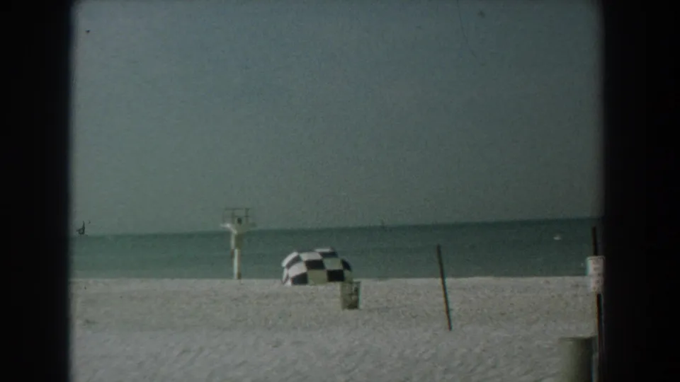 Yorktown, Virginia beach in 1958, showing a mostly empty shoreline with a checkered umbrella, posts, and calm water beyond the sand.