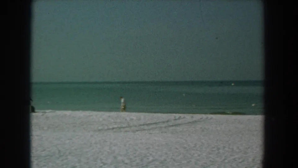 Yorktown beach view with broad pale sand, calm ocean, hazy horizon, gulls, and a distant person in swimwear near the shoreline.