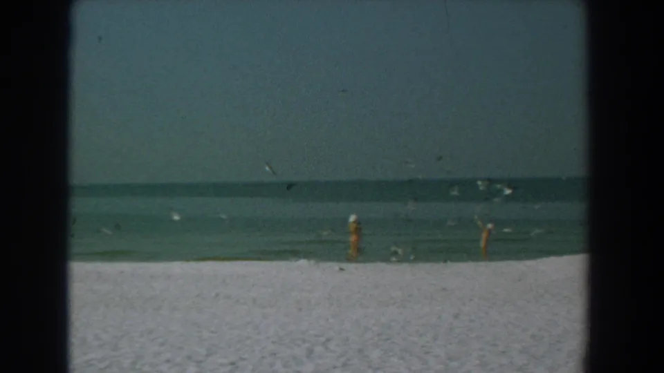 Distant beachgoers and birds appear along the 1958 Yorktown shoreline, with grain, scratches, and soft 8mm color.