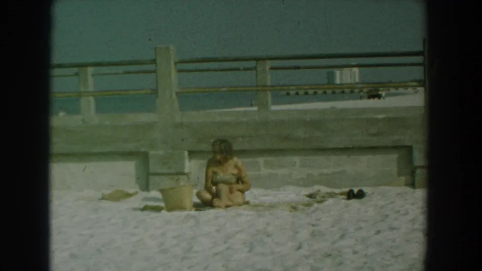 The final frame holds on the 1958 Yorktown beach setup, showing the seated woman, bucket, towel, shoes, railing, and water in soft 8mm color.