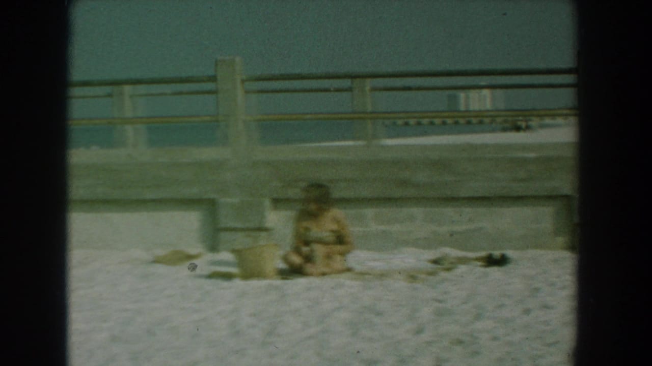 Woman seated on sand near a concrete pier wall at a beach.