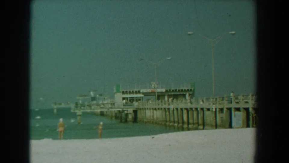A 1958 Yorktown shoreline view shows the pier, calm water, tall lamps, and beachgoers spaced along the sand.