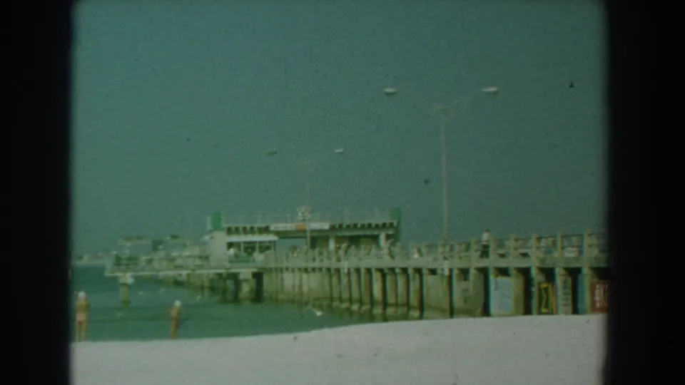 Yorktown, Virginia beach footage shows a long pier, pale sand, distant beachgoers, and small birds against a hazy 1958 sky.