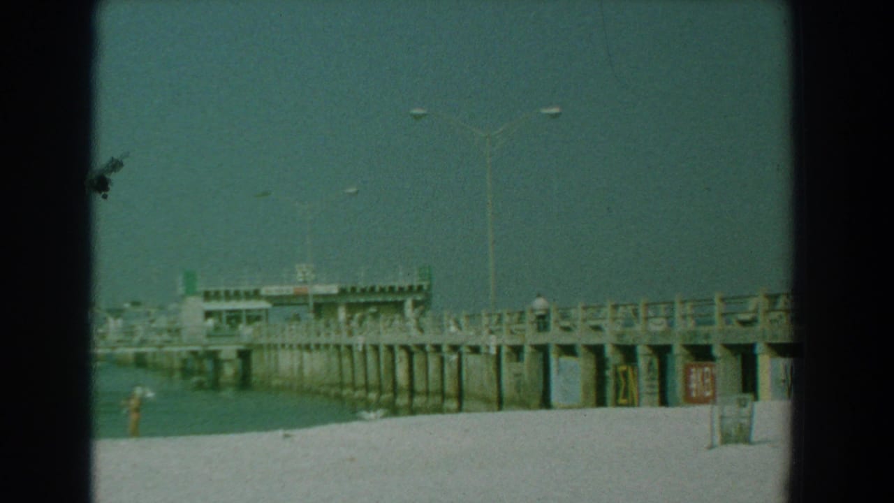 Concrete pier extending over calm water with sandy beach in the foreground.