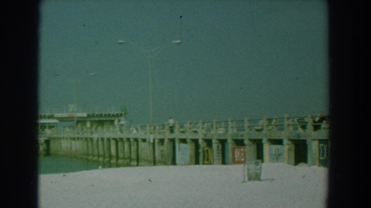 Pier with railings, light poles, calm water, and sandy foreground.