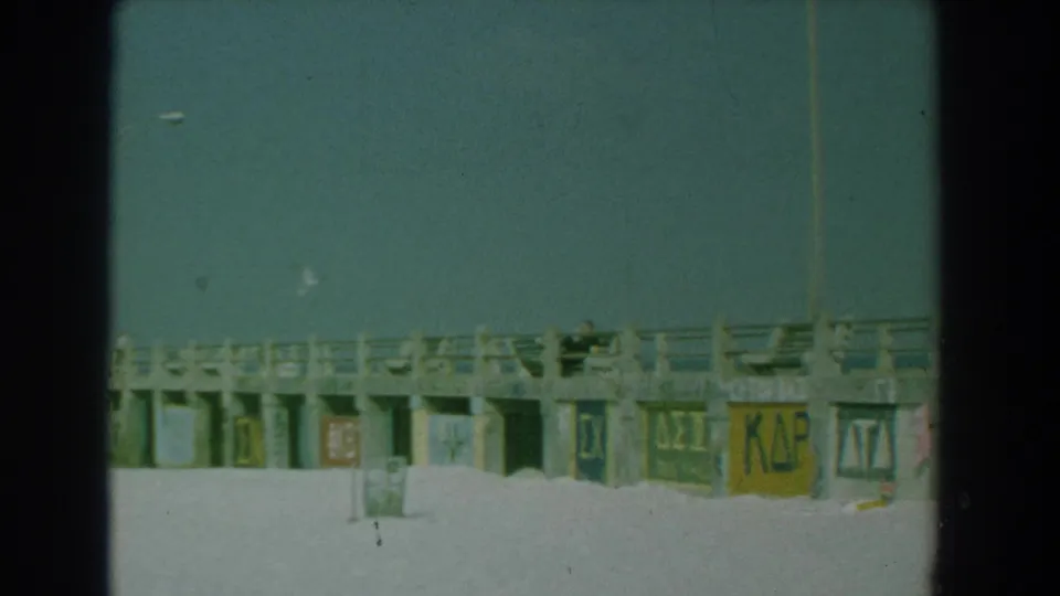 1958 Yorktown, Virginia frame with Greek letter signs painted on the pier wall and a distant person near the railing.
