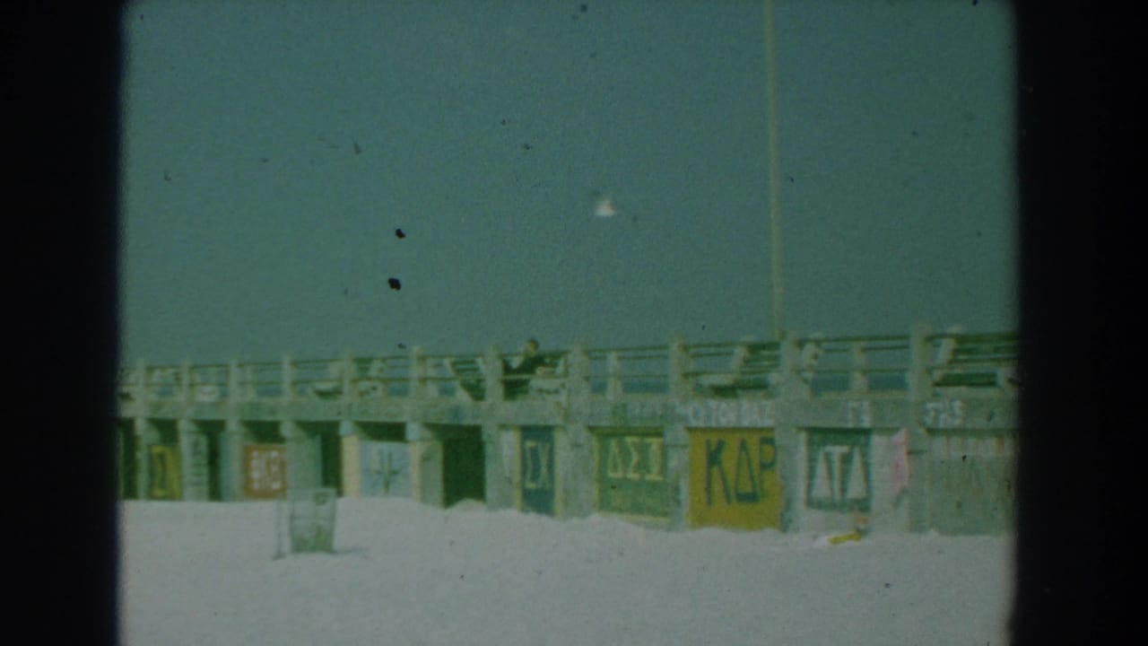 Concrete boardwalk railing above sand with painted Greek-letter markings on the pillars.