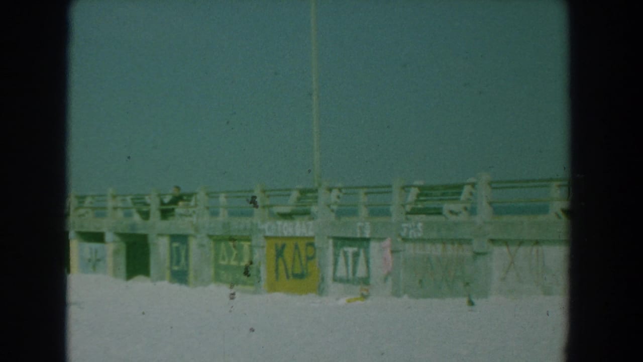 Boardwalk railing and painted pillar signs seen from the beach with sand in the foreground.