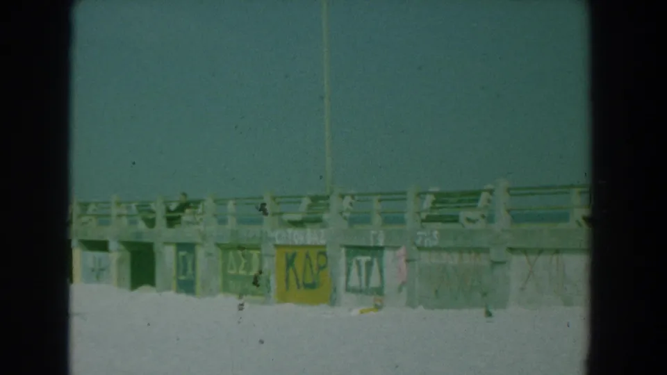 Beach-level view of the Yorktown boardwalk, with painted fraternity-style Greek letters visible on concrete supports.