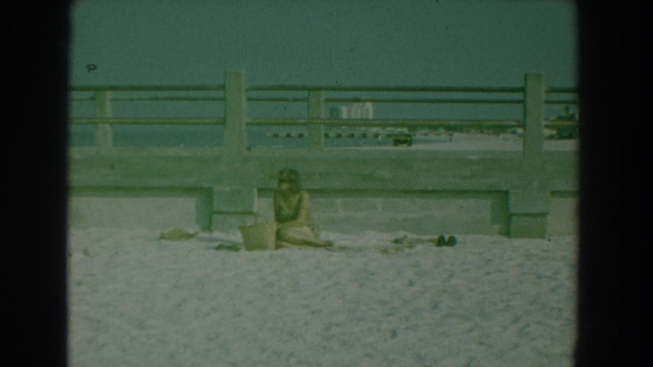 Woman on sand under a concrete walkway with the water and distant shore behind her.