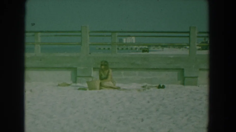 Yorktown beach frame from 1958 showing a seated woman near a basket, with concrete railings and water in the background.