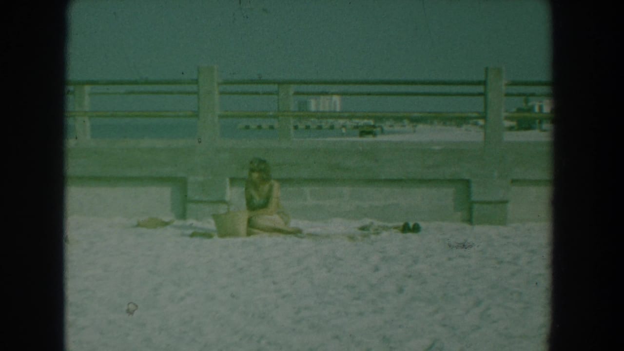 Woman sitting on sand near concrete pier railing with shoes nearby.