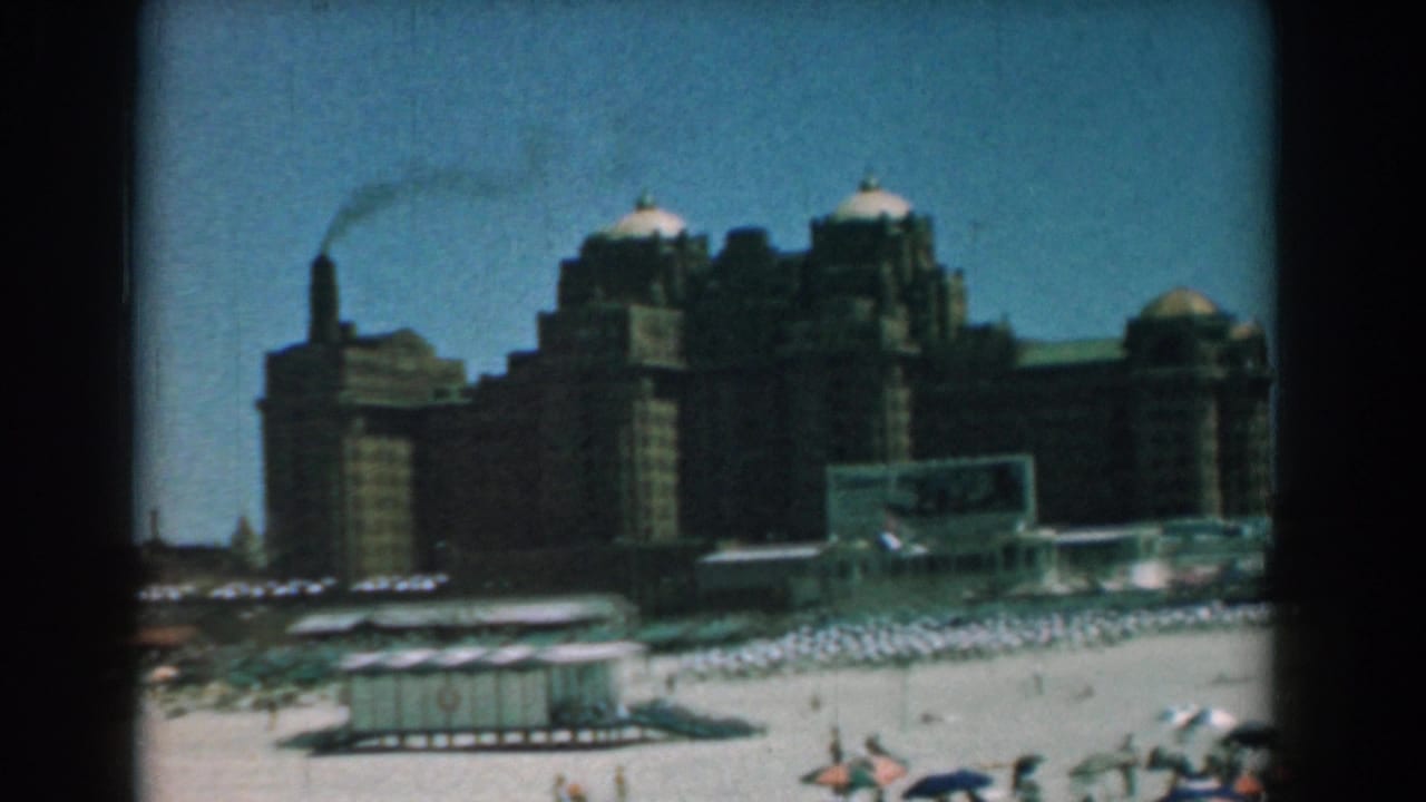 Beach scene with rows of umbrellas, a small hut, large buildings, and smoke drifting in the sky.