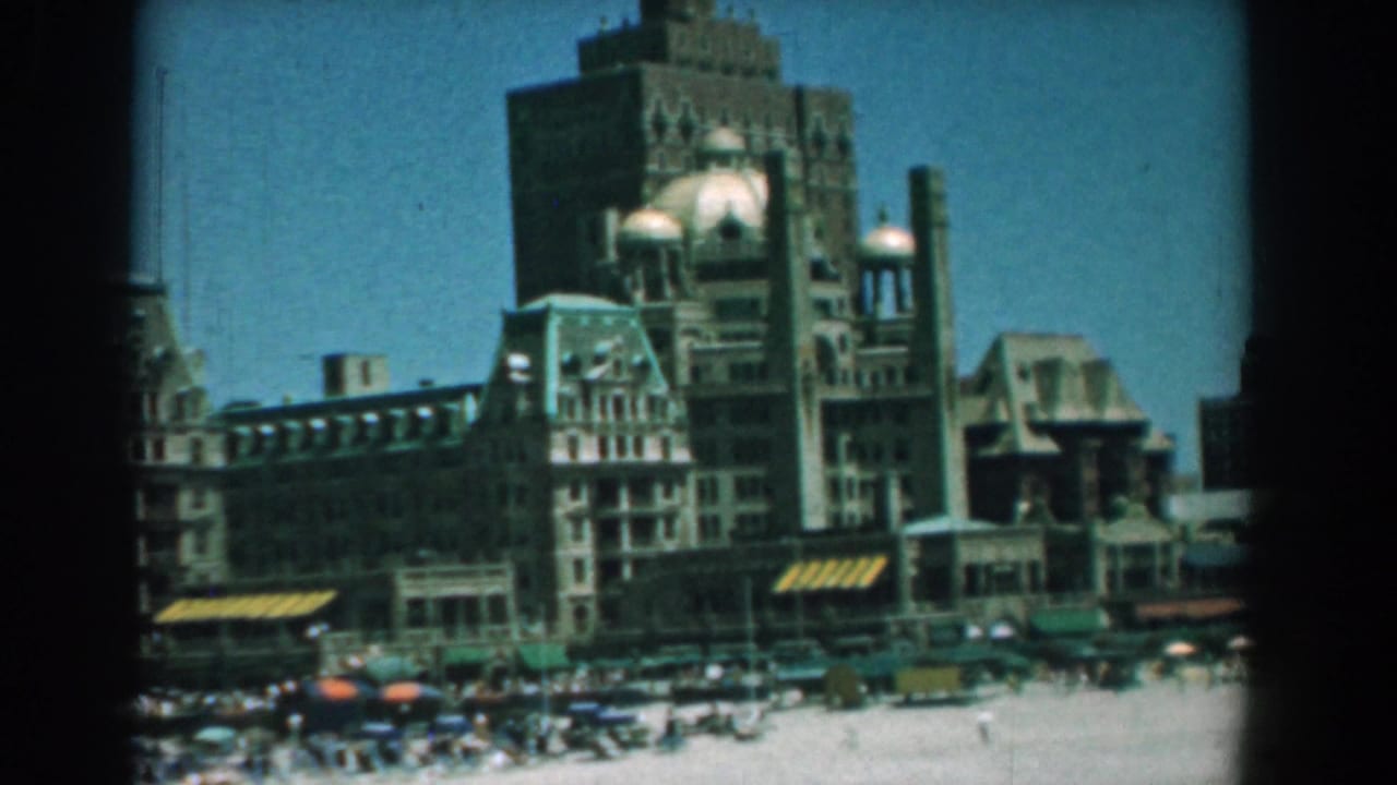 Waterfront building with towers above a crowded beach under a blue sky.