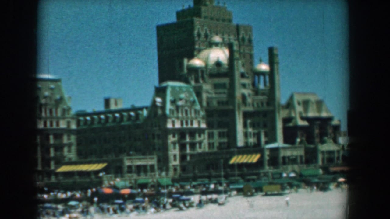 Similar beachfront view with a large building, beach crowd, and striped shade structures.