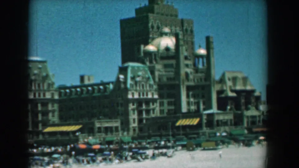 1958 Yorktown, Virginia frame with a visitor-shot view of the waterfront building and busy beach area in soft 8mm color.