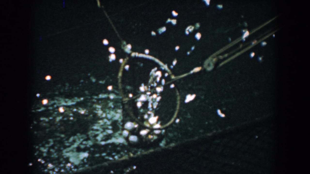 Circular fishing net lifts from dark water with bright splashes and metal support rods.