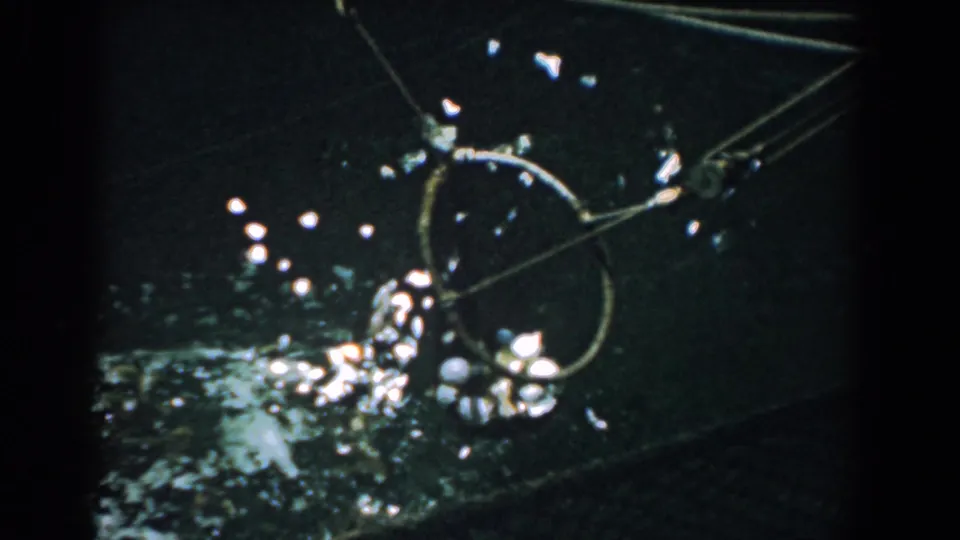 1958 Yorktown 8mm frame showing the circular fishing net tilted over dark water with reflective droplets and small catch visible.